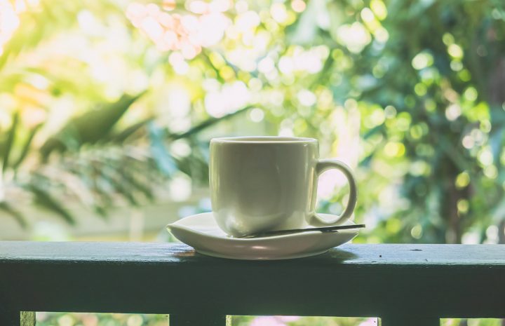 Une tasse de café posée sur une terrasse invite à profiter d’un moment de calme et de détente au cœur de la nature. Baignée d’une douce lumière et entourée de verdure, cette image chaleureuse évoque une pause paisible, un agréable début de journée et le plaisir de prendre le temps de savourer l’instant présent.