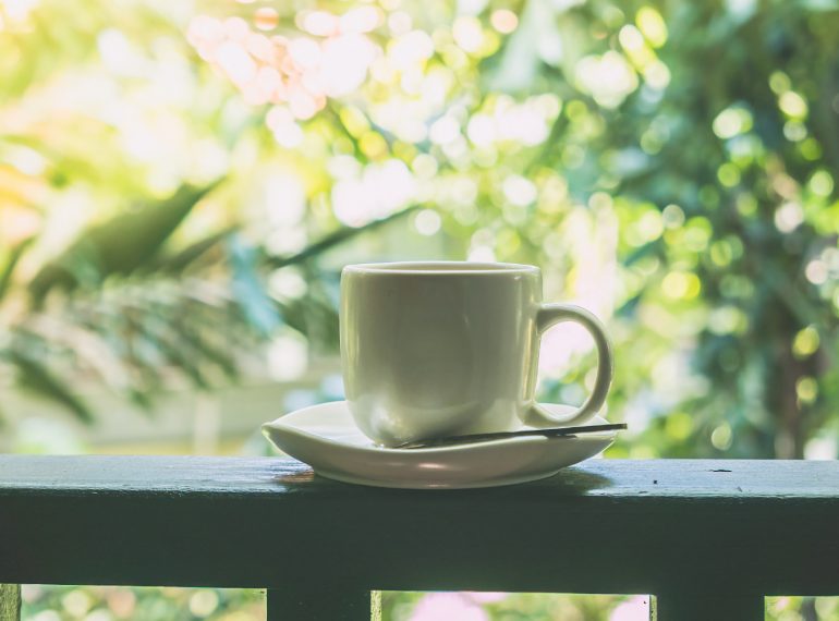 Une tasse de café posée sur une terrasse invite à profiter d’un moment de calme et de détente au cœur de la nature. Baignée d’une douce lumière et entourée de verdure, cette image chaleureuse évoque une pause paisible, un agréable début de journée et le plaisir de prendre le temps de savourer l’instant présent.